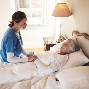 Shot of a young nurse chatting with a senior woman in bed at a retirement home.